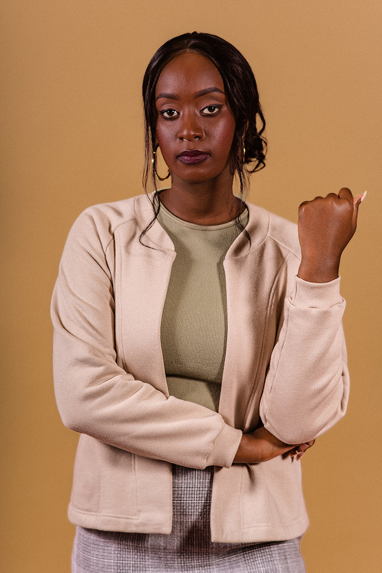 Beije background, model stanting up, lookng at the camera, golden earrings short gray skirt, cottom fleece jacket, original
